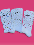 Three white Nike crew socks embellished with rhinestones, arranged side by side on a vibrant pink background.